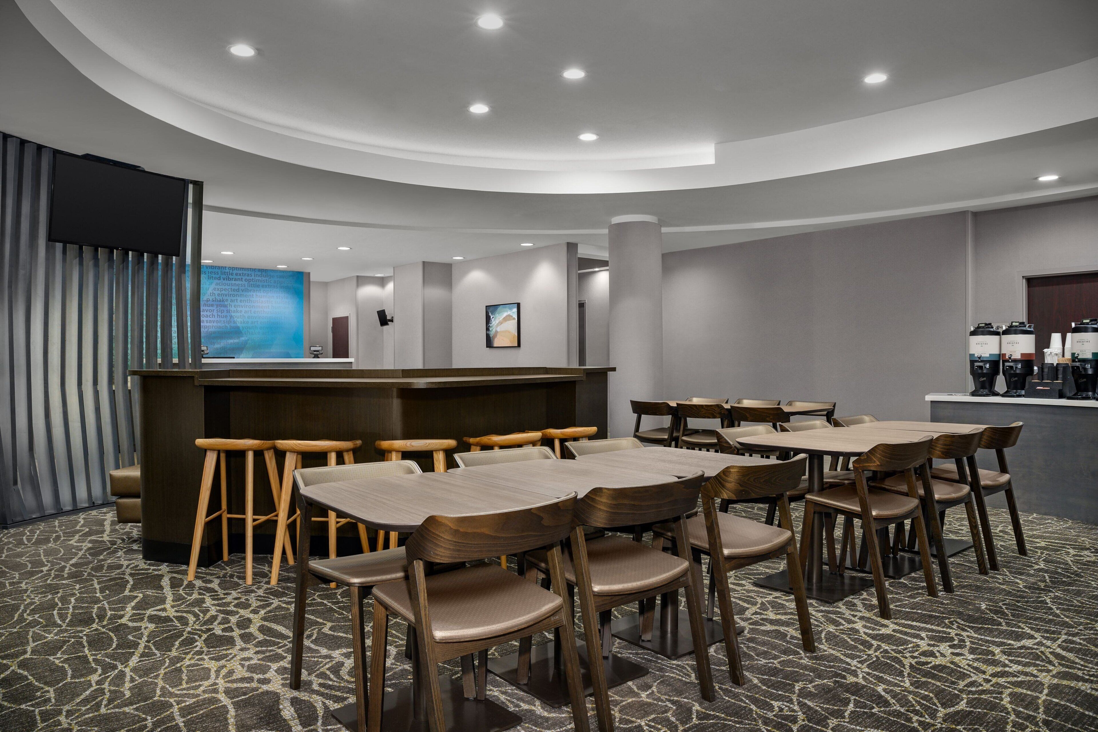 A modern hotel lobby with a curved reception desk, wooden chairs, and tables.
