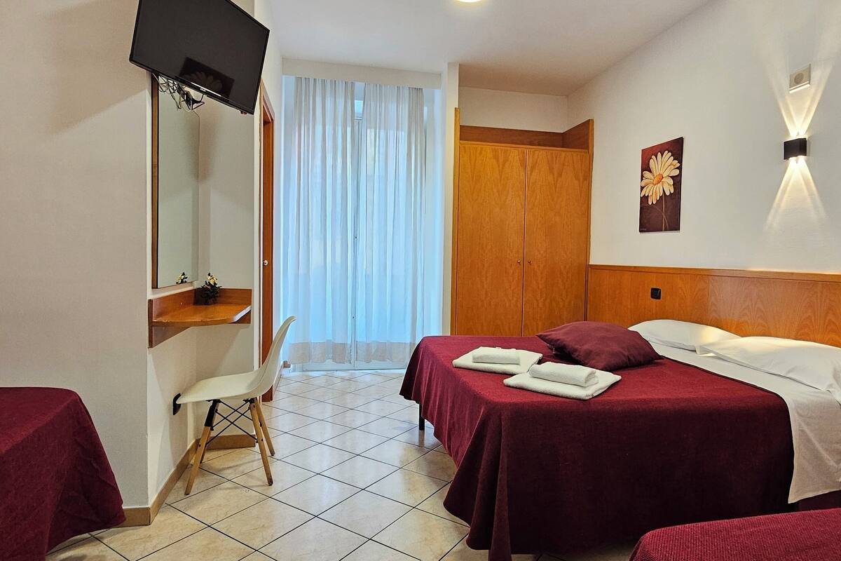 A hotel room with two beds, a desk, a chair, and a TV.