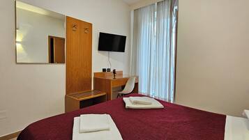 A hotel room with a bed, a desk, a chair, a television, and a window with curtains.