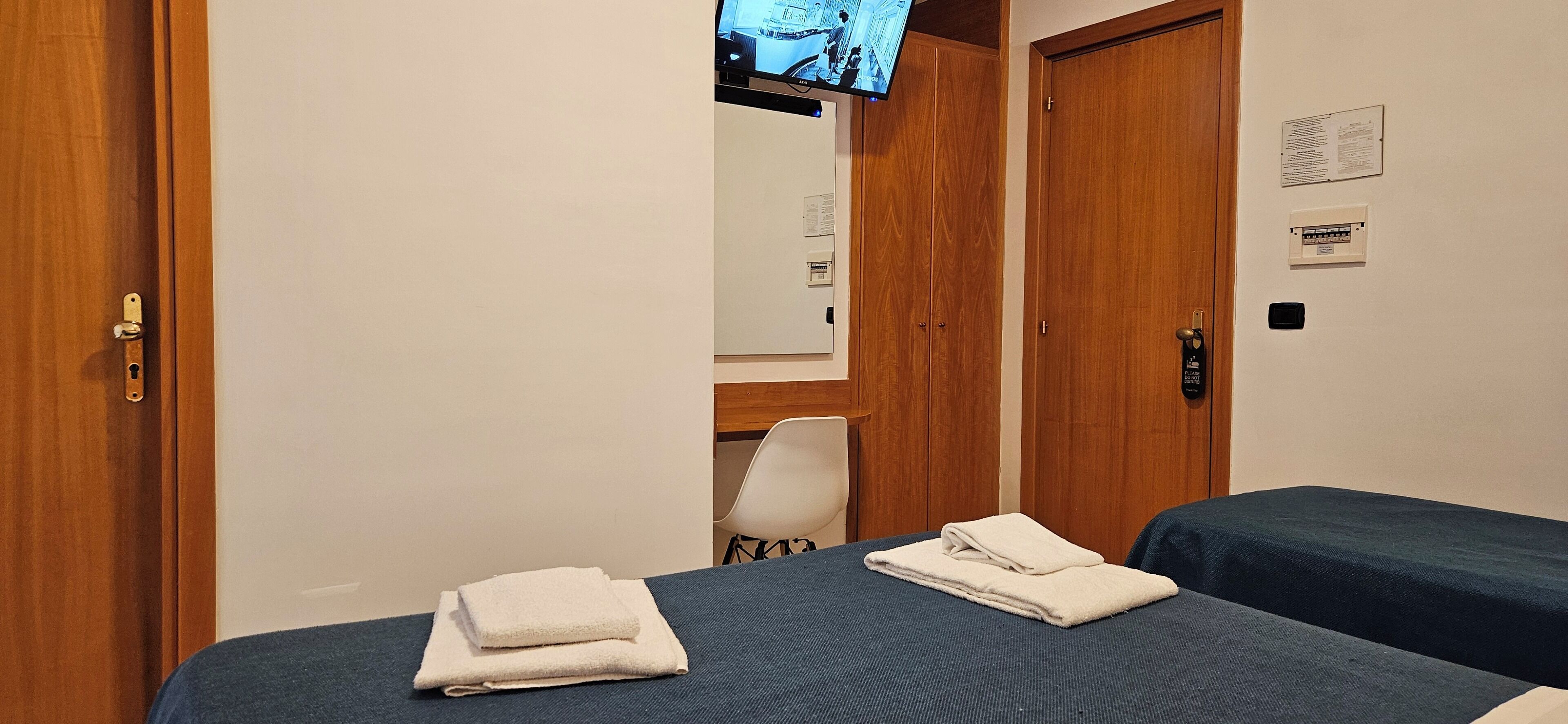 A hotel room with two beds, a TV mounted on the wall, and a wooden door.