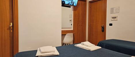 A hotel room with two beds, a TV mounted on the wall, and a wooden door.