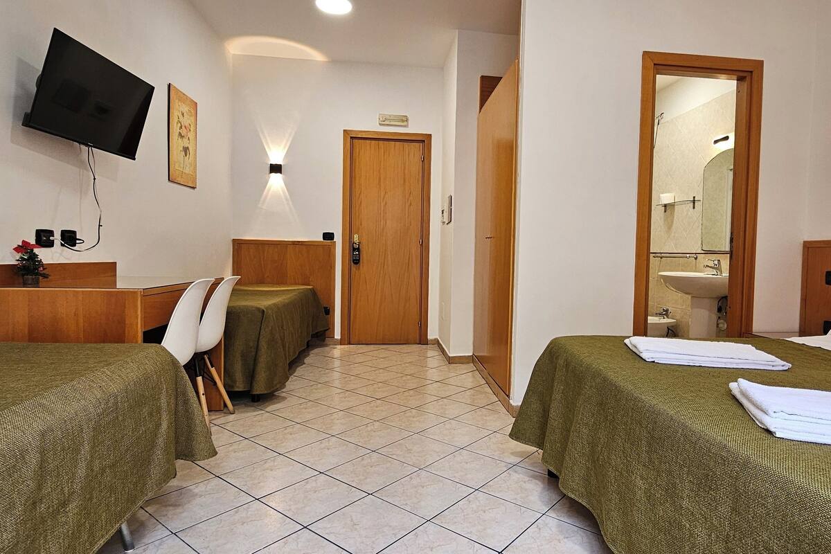 A hotel room with two beds, a desk with a chair, a television, and a bathroom visible through an open door.