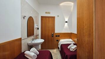 A small, clean bathroom with a sink, mirror, and two beds with towels.