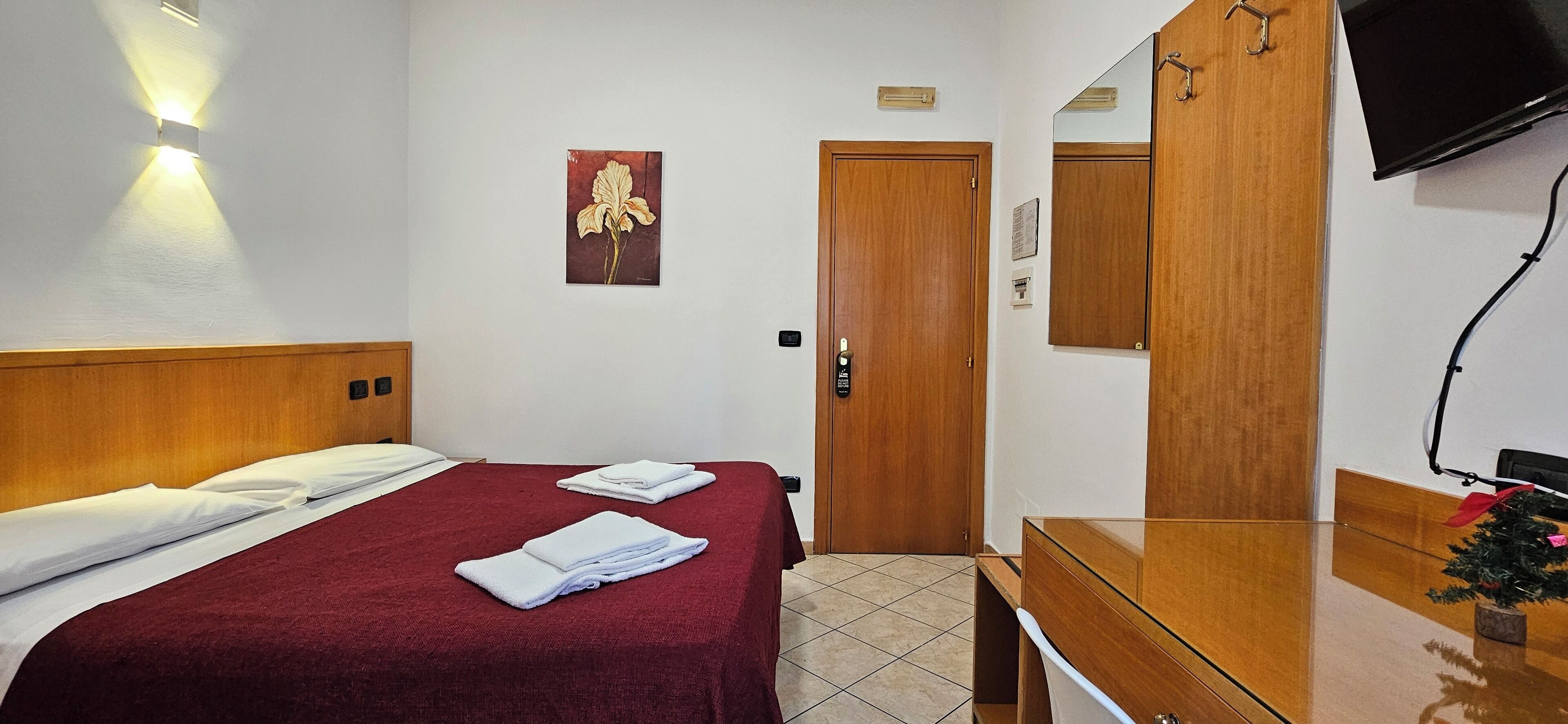 A hotel room with a bed, a wooden wardrobe, a mirror, and a television.