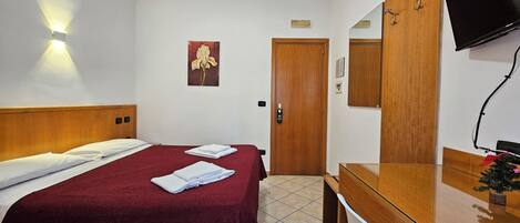 A hotel room with a bed, a wooden wardrobe, a mirror, and a television.