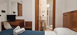 Habitación de hotel con cama, escritorio con computadora, espejo, baño con lavamanos e inodoro, y ducha.