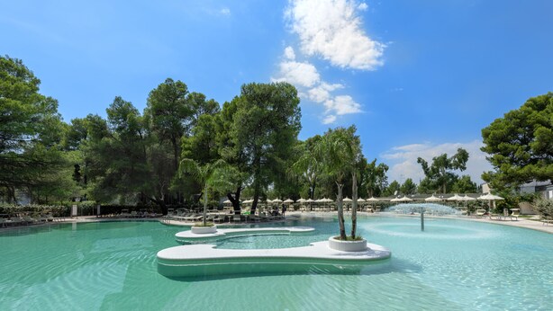 A pool area with multiple water features, surrounded by trees and lounge chairs. - Ethra Reserve - Alborèa 5* (Castellaneta)