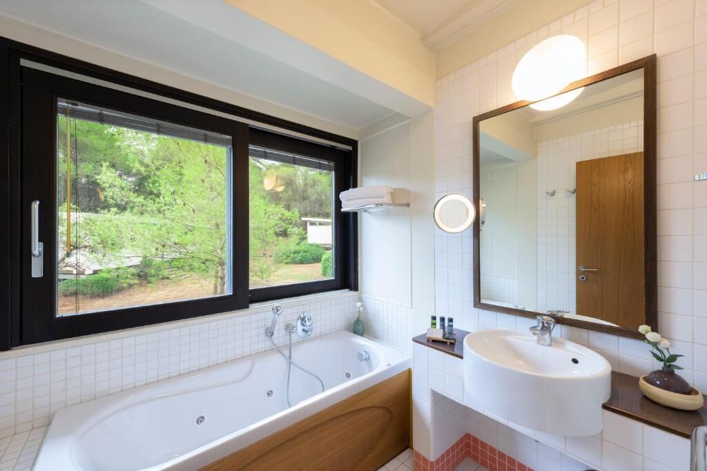 Un baño moderno con una bañera grande, un lavamanos, un espejo y una ventana con vistas a zonas verdes.