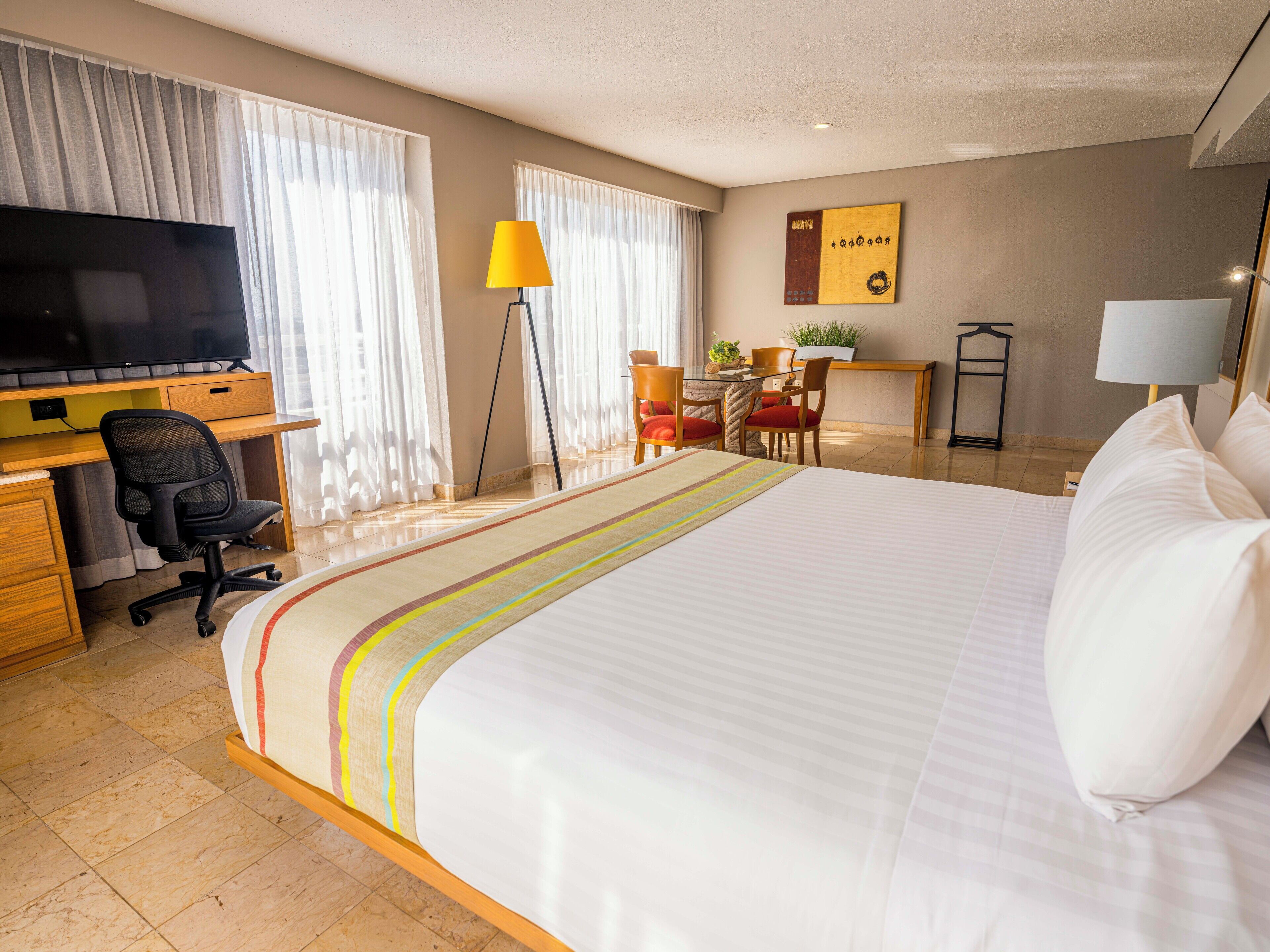 Een hotelkamer met een groot bed, een bureau met een computer, een televisie en een zithoek.