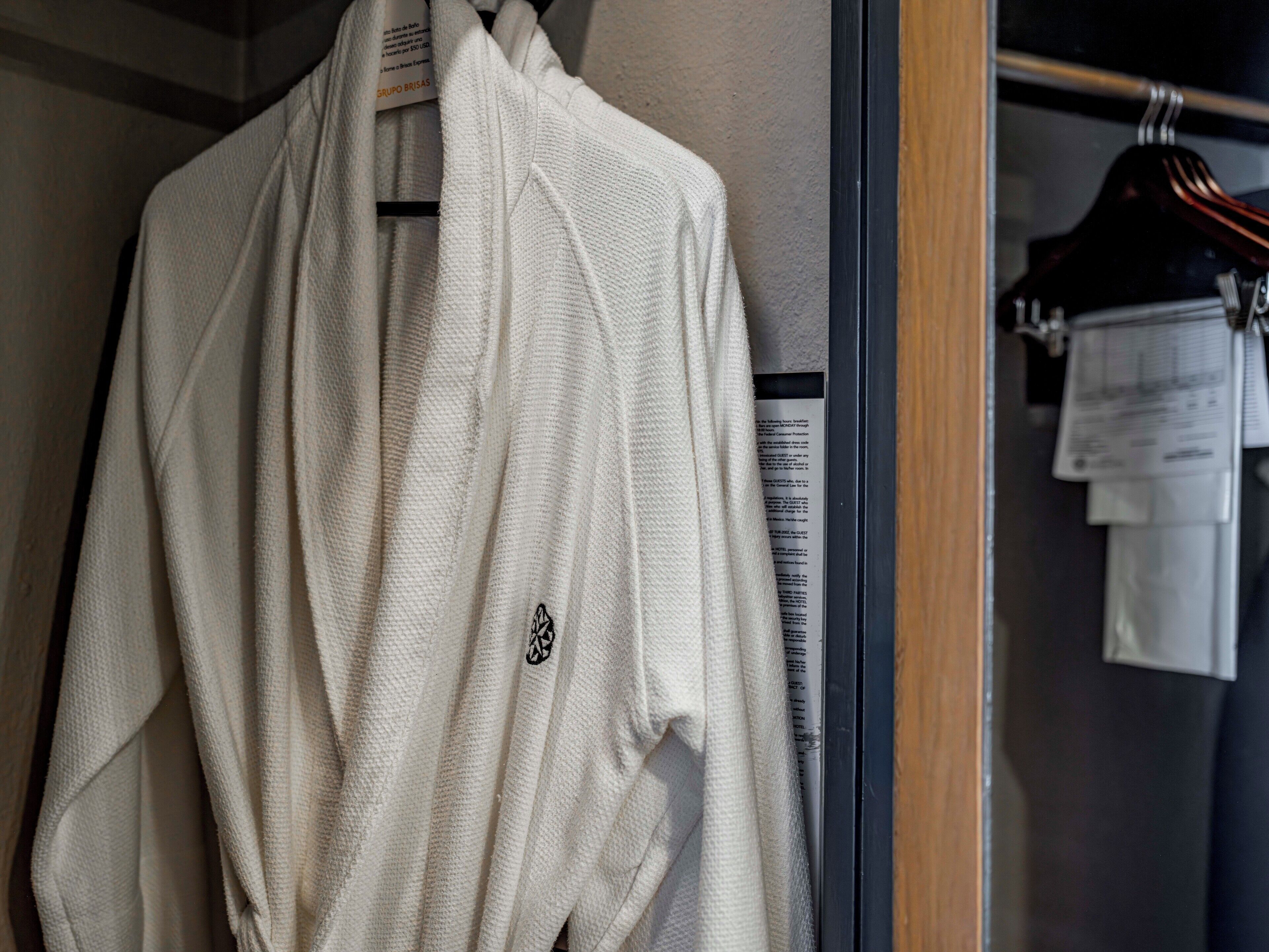 Une robe blanche est suspendue à un portant dans un placard dont la porte est en bois et qui est muni d’un cintre noir.