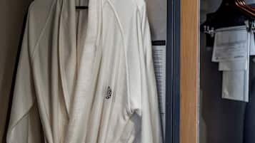 Une robe blanche est suspendue à un portant dans un placard dont la porte est en bois et qui est muni d’un cintre noir.