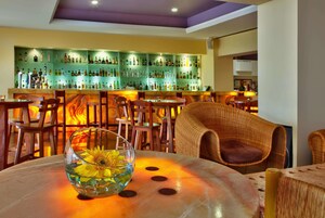 Zona de bar con diversas opciones de asientos, barra con una variedad de botellas y una mesa con un bol de vidrio con flores.