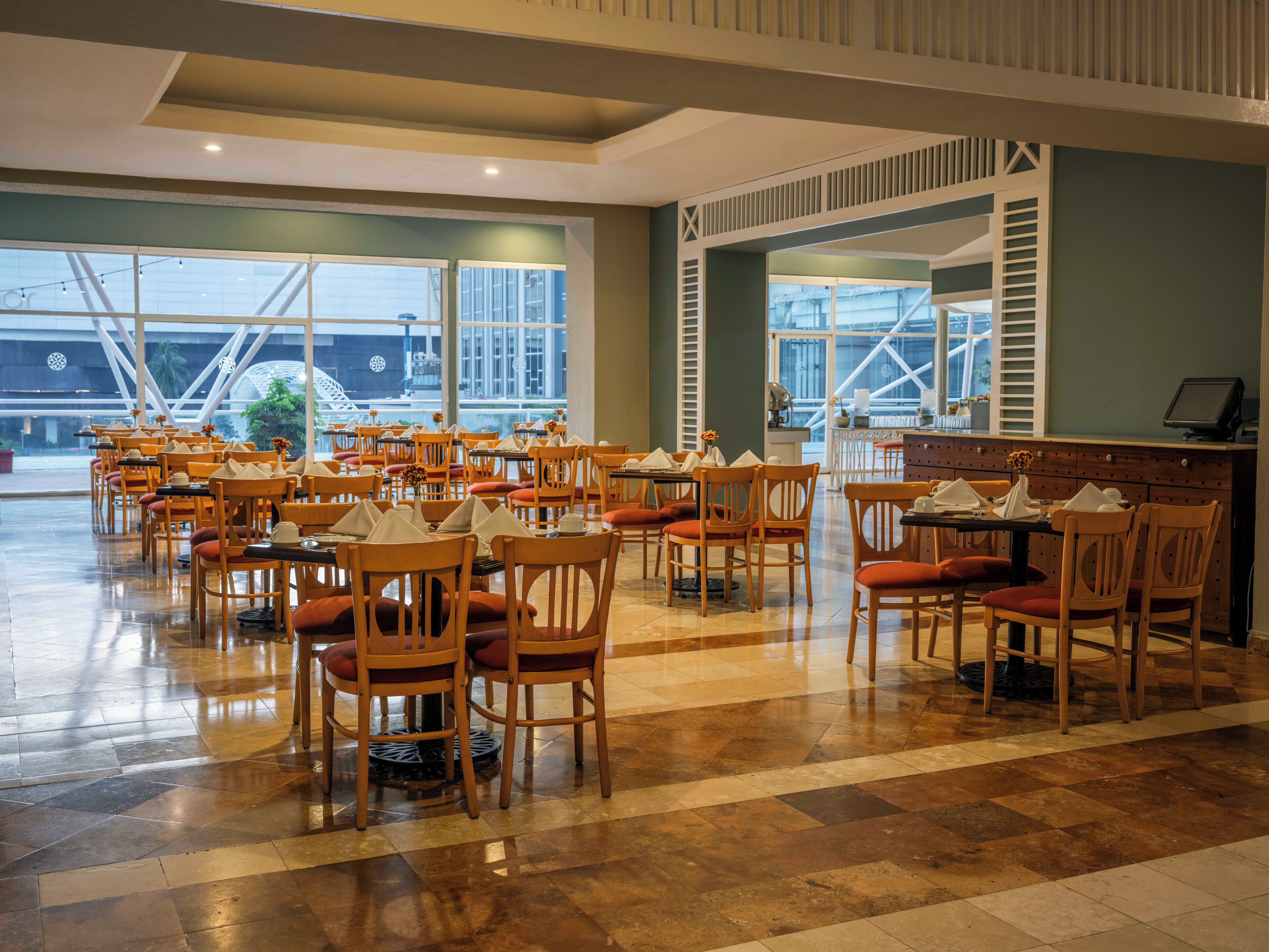 Ein geräumiges Restaurant mit mehreren Tischen und Stühlen, großen Fenstern und einem modernen Interieur.