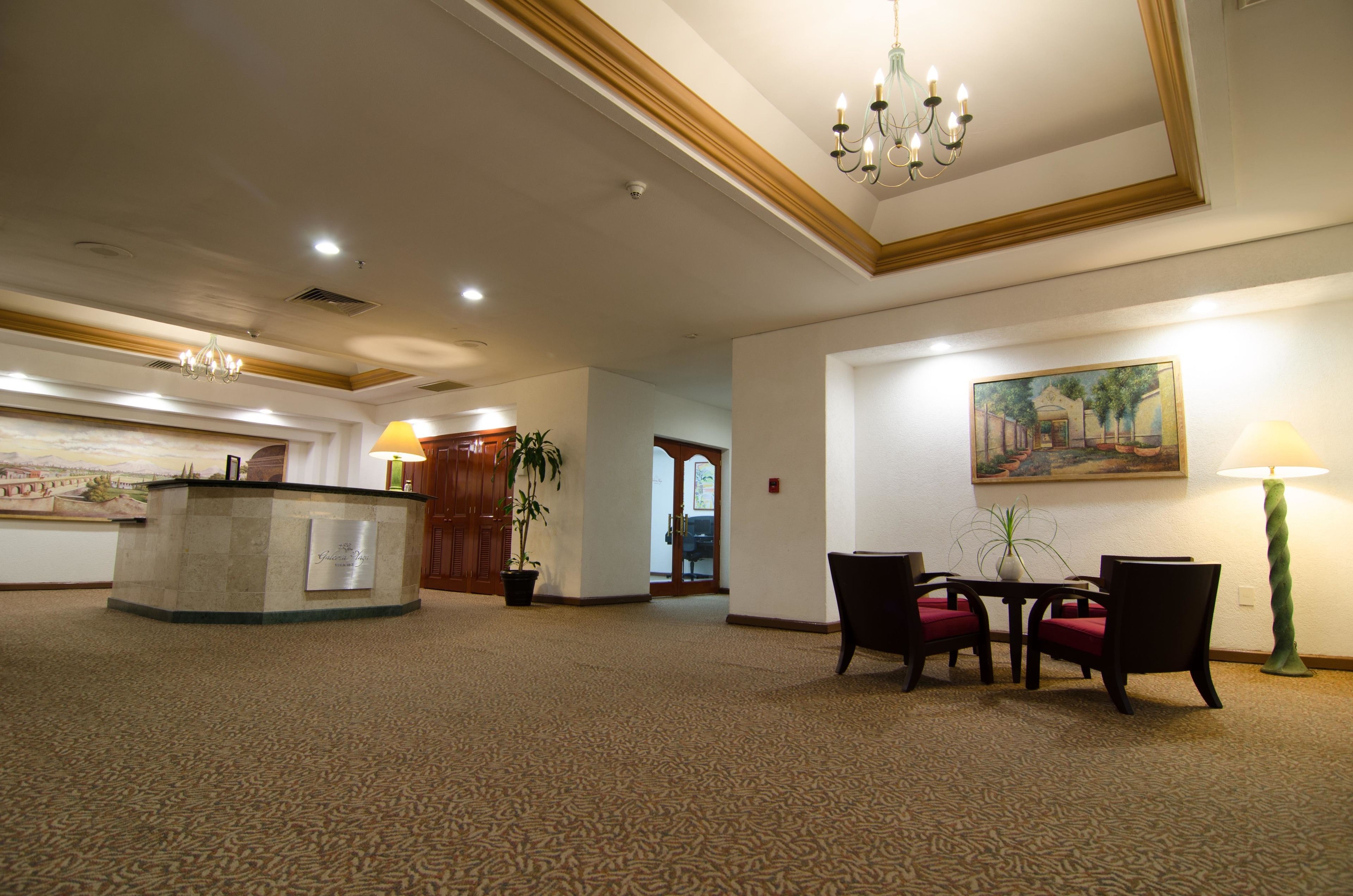 Een hotellobby met een receptiebalie, een kroonluchter, een schilderij, een tafel met stoelen en een potplant.