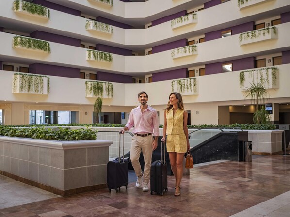 Un lobby espacioso de diseño moderno, con un jardín interior central, varios pisos con balcones y un suelo de mármol.