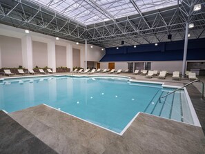 Une piscine intérieure dotée d’un toit en verre, entourée de chaises longues et recouverte d’un sol carrelé.