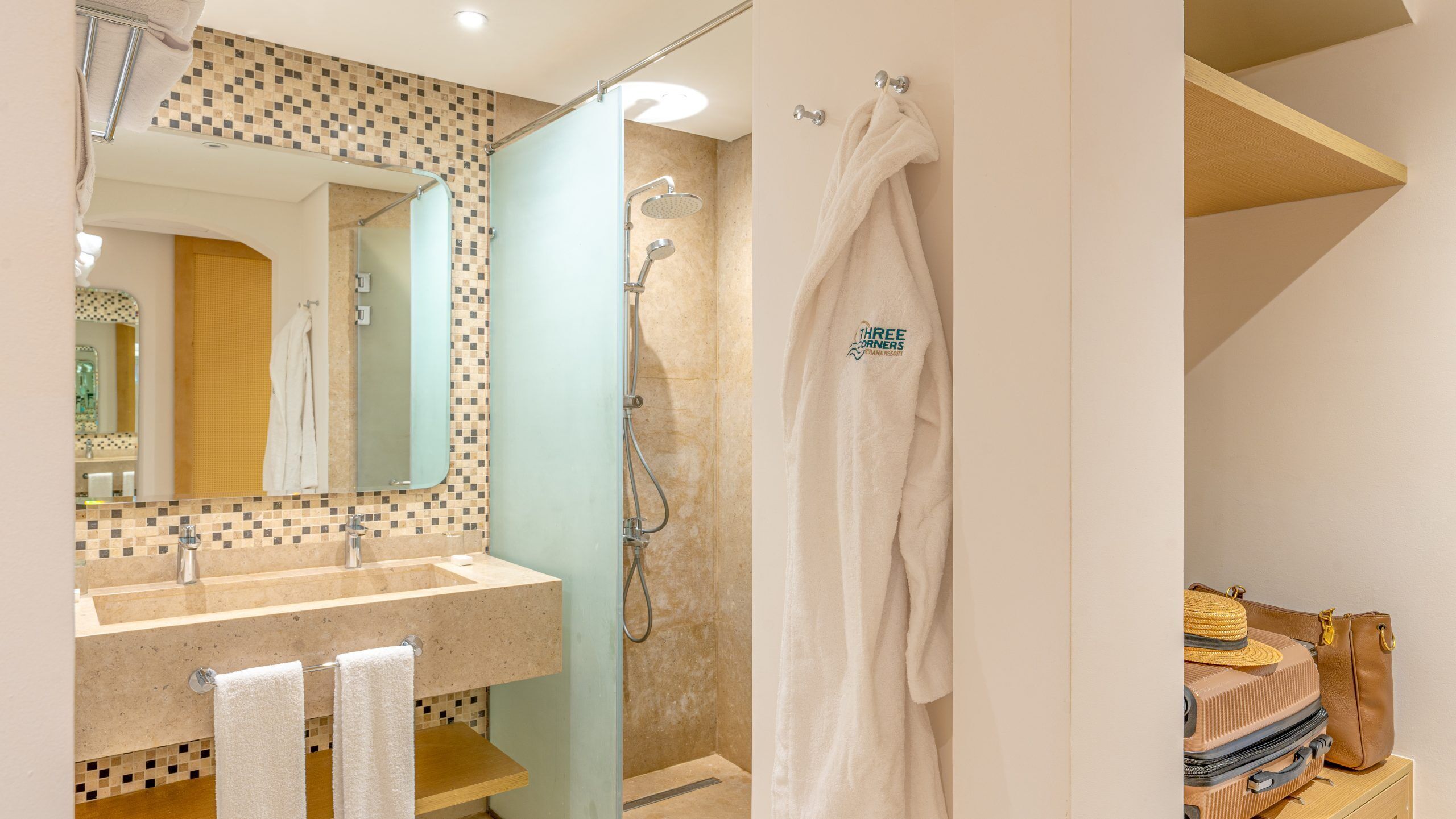 Une salle de bain avec un mur recouvert de carreaux, un lavabo, un miroir, une douche avec une porte en verre et un porte-serviettes.