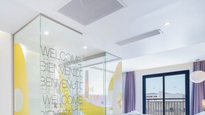 A modern hotel room with a glass partition featuring a welcome message, a bed with a patterned bedspread, a balcony with a view, and a large window with curtains. - The Purple Hotel by Ibiza Feeling - Adults only (Sant Antoni de Portmany)