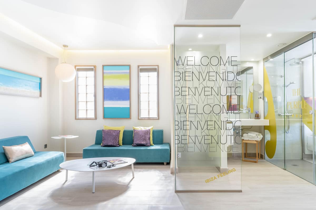 Un salon moderne avec un canapé, une table basse et une cloison en verre sur laquelle est inscrit le mot « BIENVENUE ».