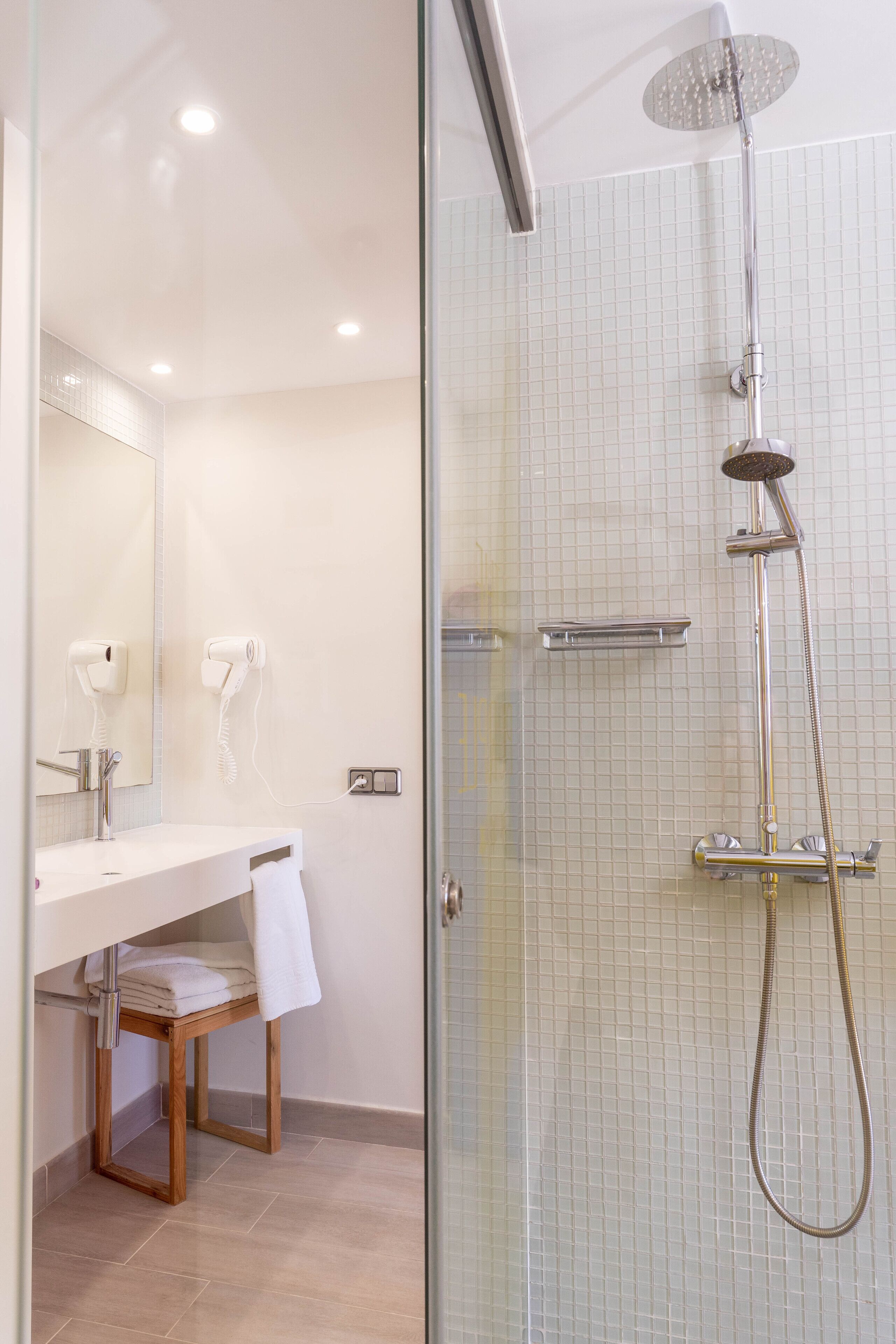 A modern bathroom with a glass shower enclosure, a wooden vanity, and a towel rack.