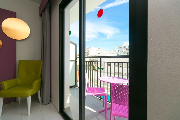 Un balcón con una silla verde, una mesa rosa y dos sillas rosadas.
