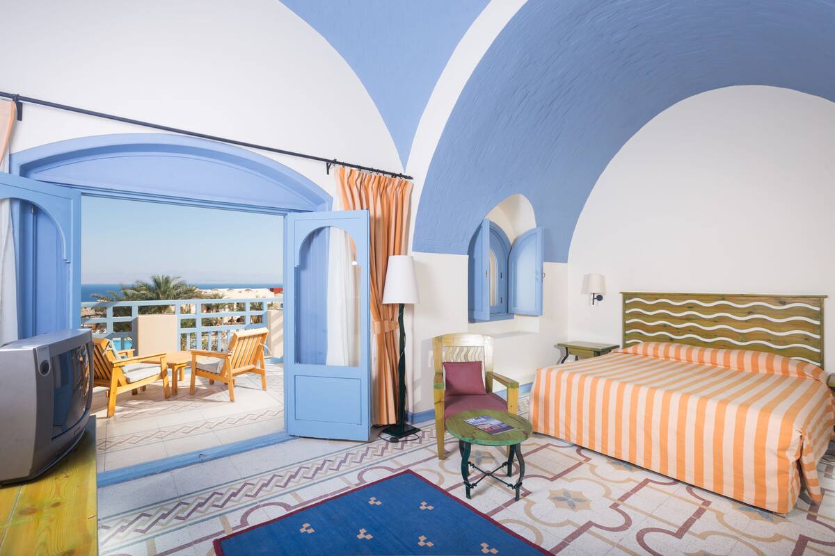 A room with a balcony, a bed, a TV, and a table with a lamp.