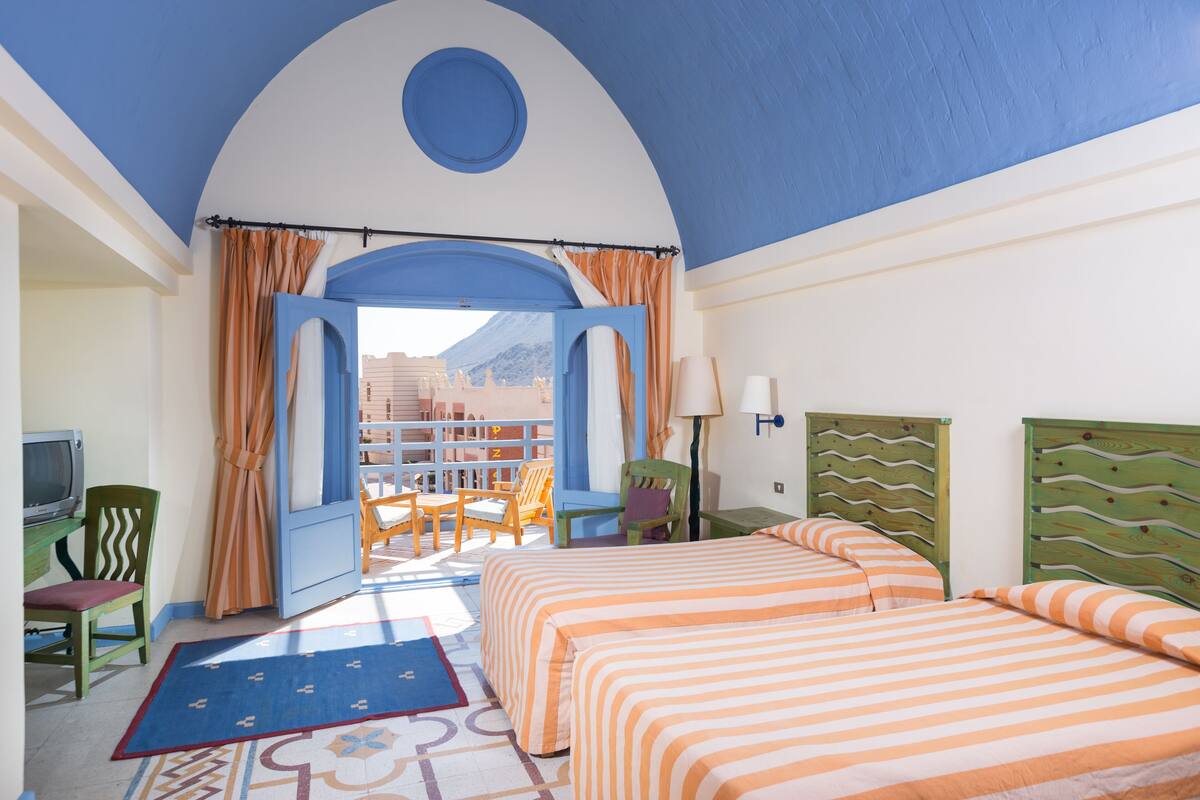 A hotel room with two beds, a TV, a desk, and a view of the mountains.