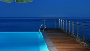 Un área junto a la piscina con una terraza de madera, sillas de descanso y vista al océano.