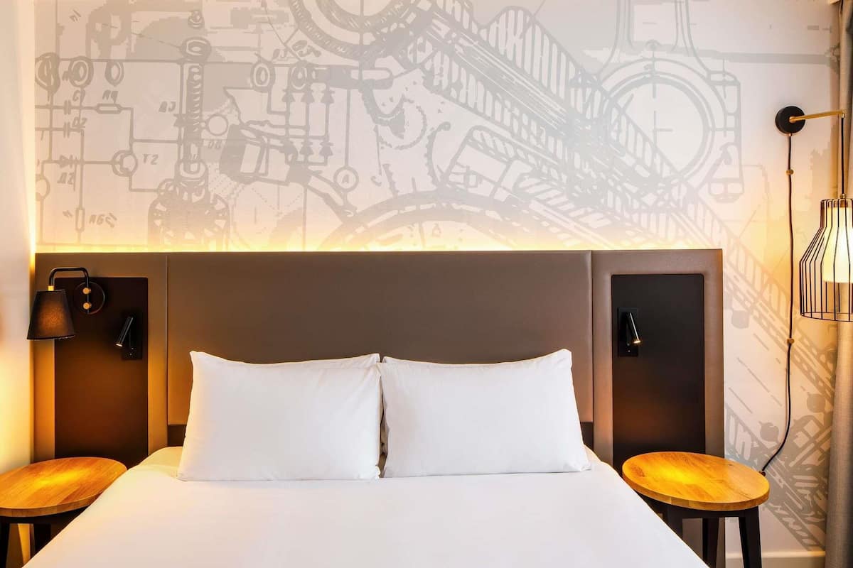 Habitación de hotel con una cama grande, dos mesitas de noche, un cabecero con un reloj y una pared con diseño moderno.