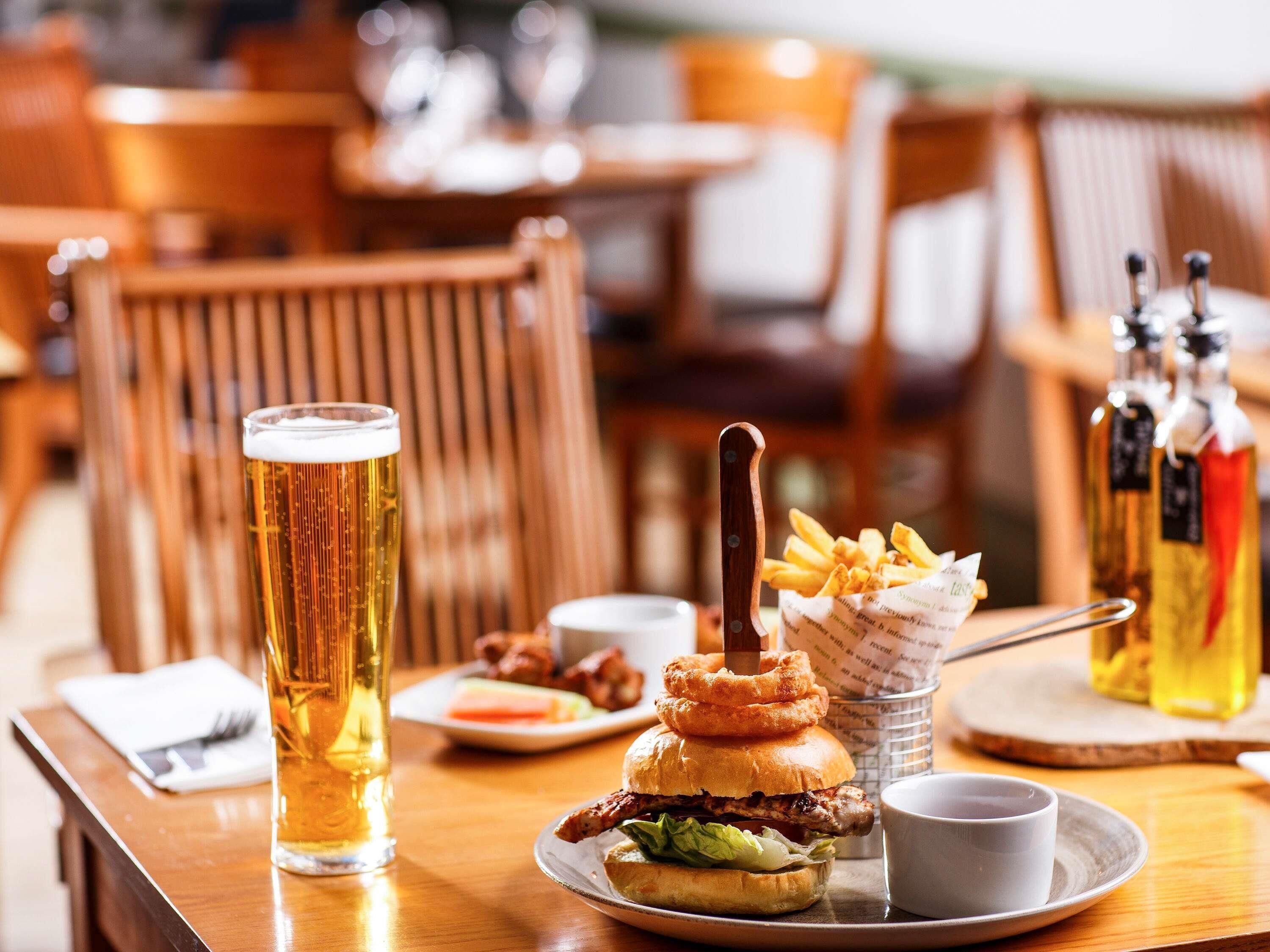 A dining table with a beer glass, a burger, fries, and condiments.