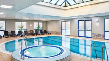 Une piscine intérieure dotée d’un jacuzzi, de chaises longues et d’une verrière.