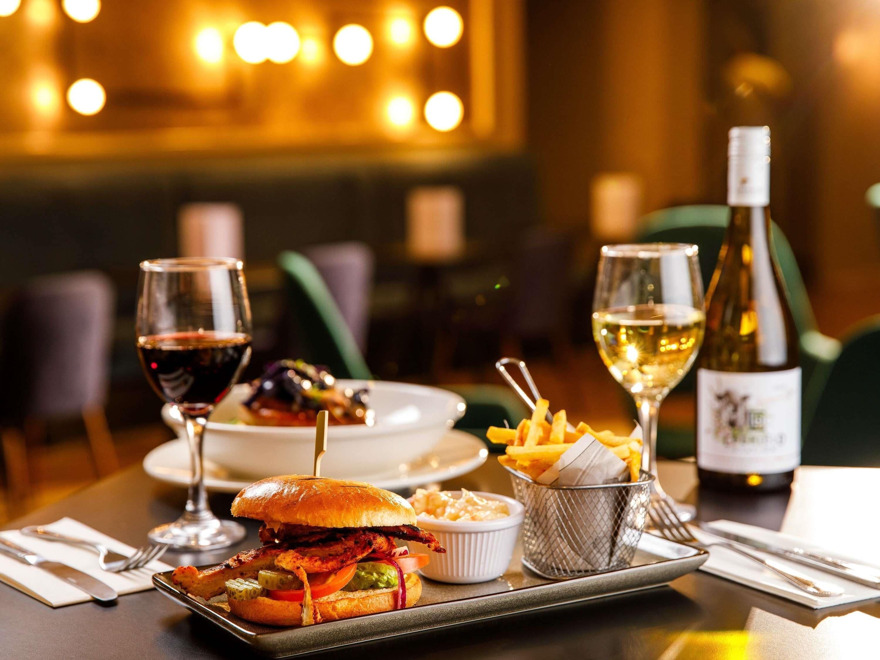 A dining table with a sandwich, fries, and wine glasses.