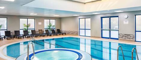 An indoor swimming pool with a hot tub, lounge chairs, and a skylight.