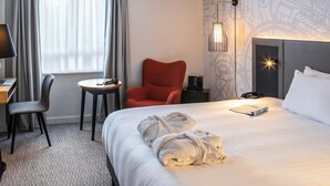 A hotel room with a bed, a desk with a laptop, a chair, a small table, and a red armchair. - Mercure Birmingham West Hotel (West Bromwich)