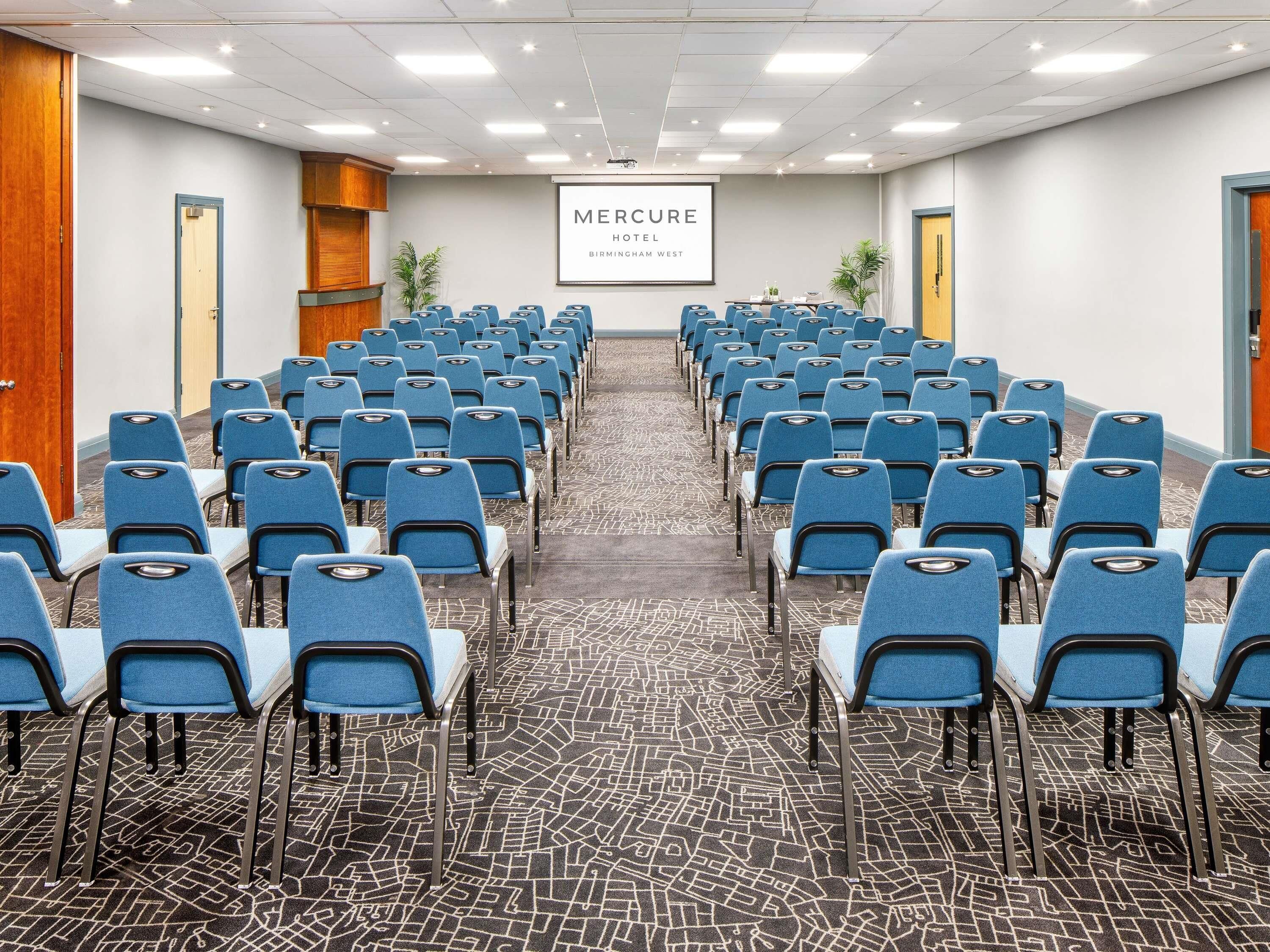 A conference room with rows of blue chairs, a carpeted floor, and a sign reading 'Mercure Hotel Birmingham'.