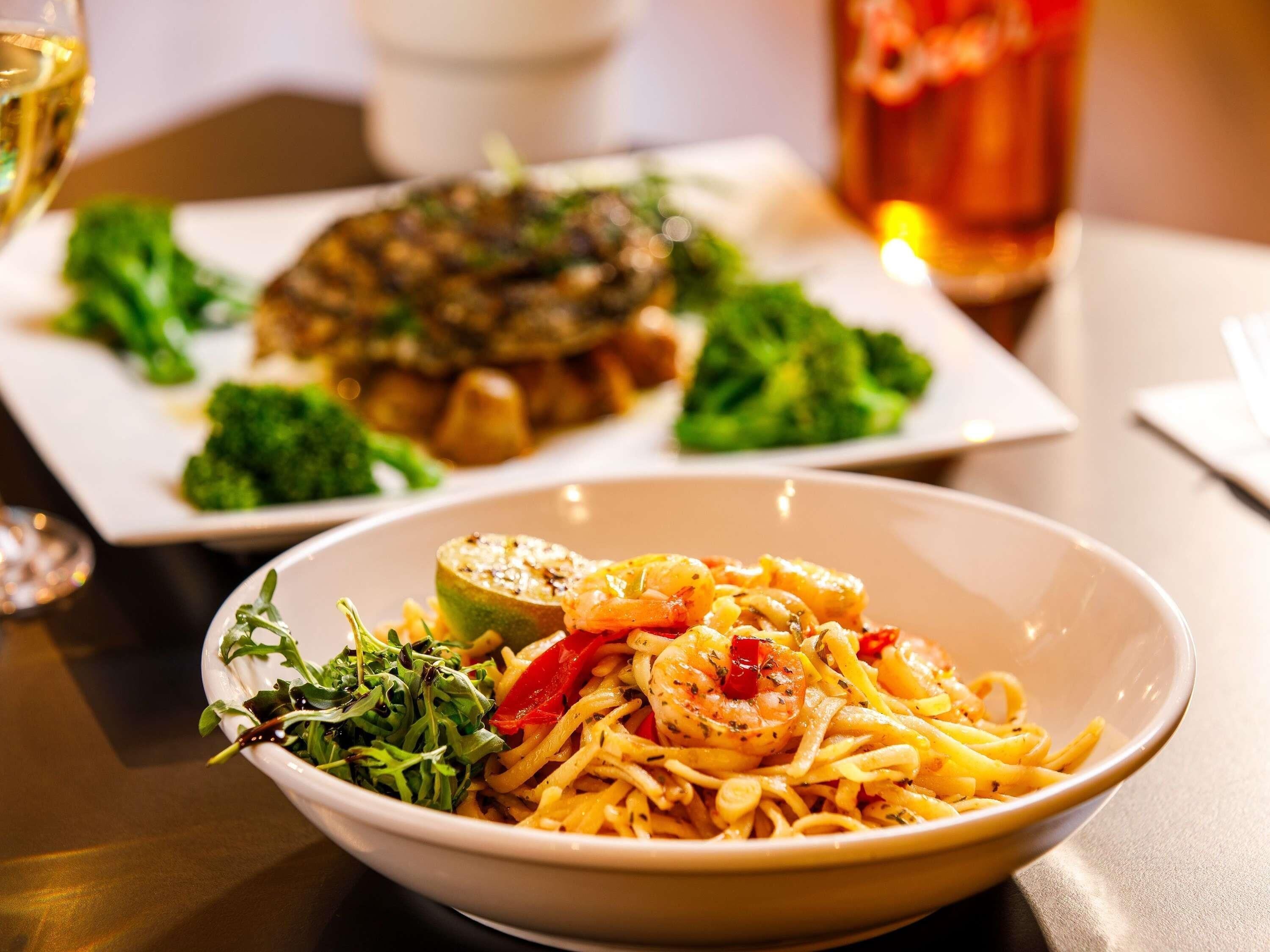 A dining table with a bowl of pasta, a plate of vegetables, and a glass of red beverage.
