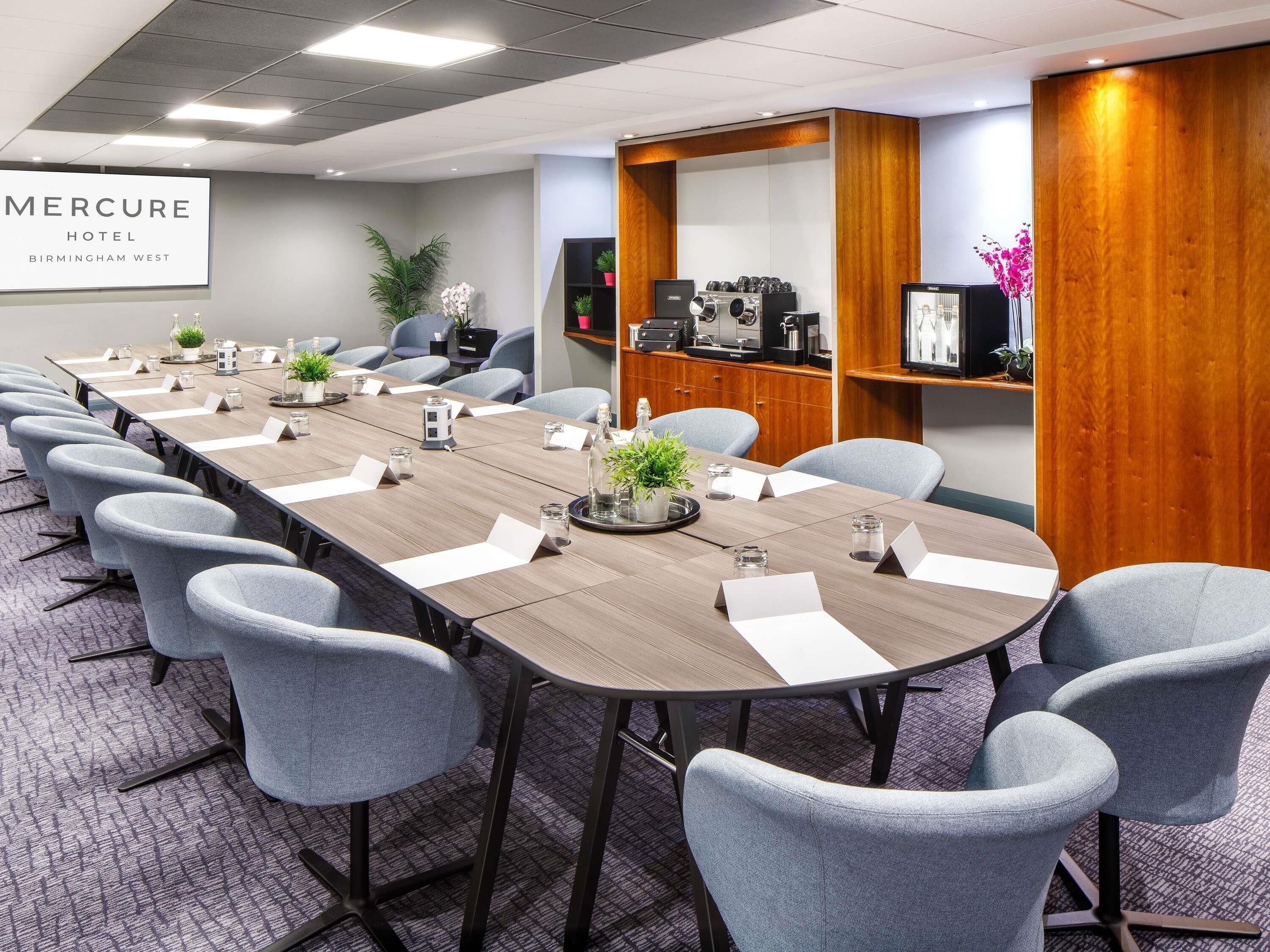 A conference room with a long table, chairs, name cards, and a wooden accent wall.