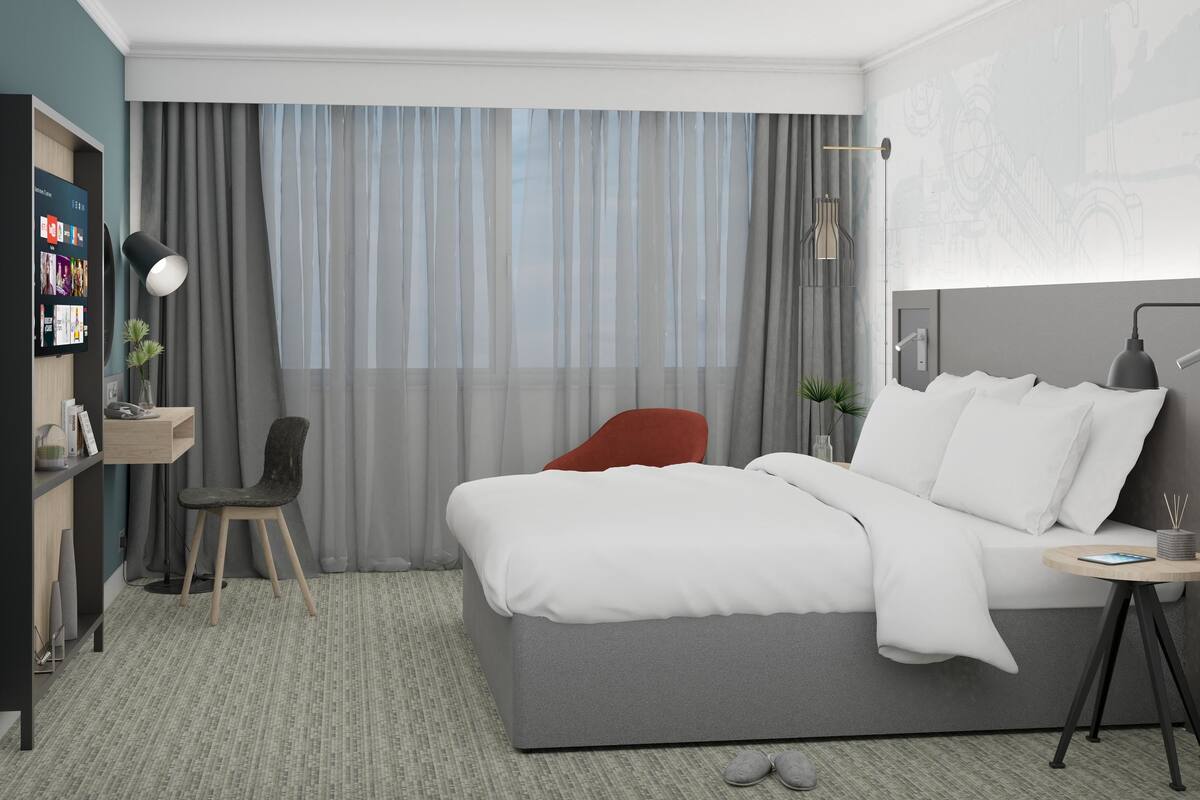 A modern hotel room with a bed, a desk, a chair, and a TV mounted on the wall.