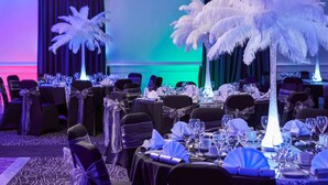 A formal dining area with tables set for a meal, chairs with bows, and a decorative feather tree centerpiece. - Mercure Birmingham West Hotel (West Bromwich)