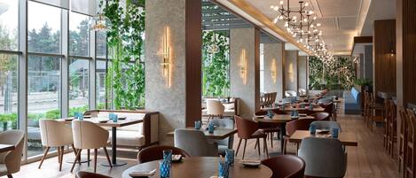 A modern restaurant with large windows, wooden tables, and chairs.
