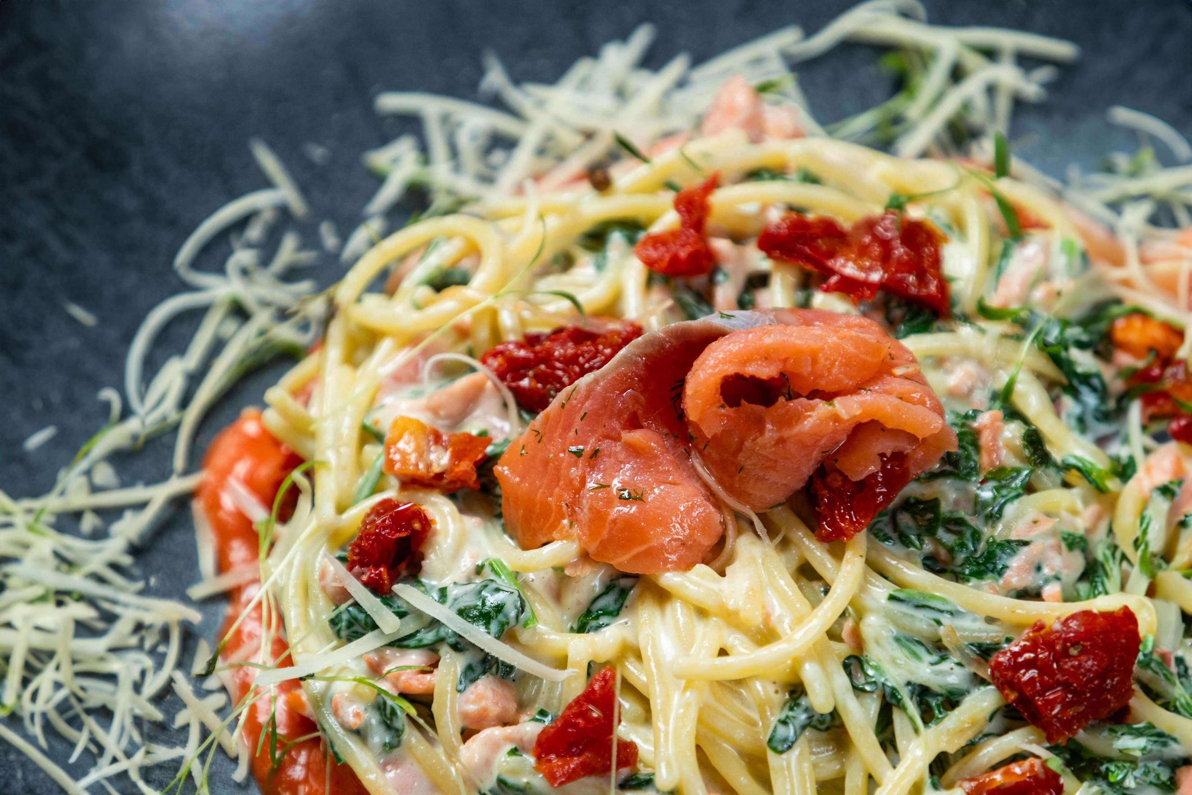 Een close-up van een pastagerecht met ingrediënten zoals zalm, kaas en kruiden.