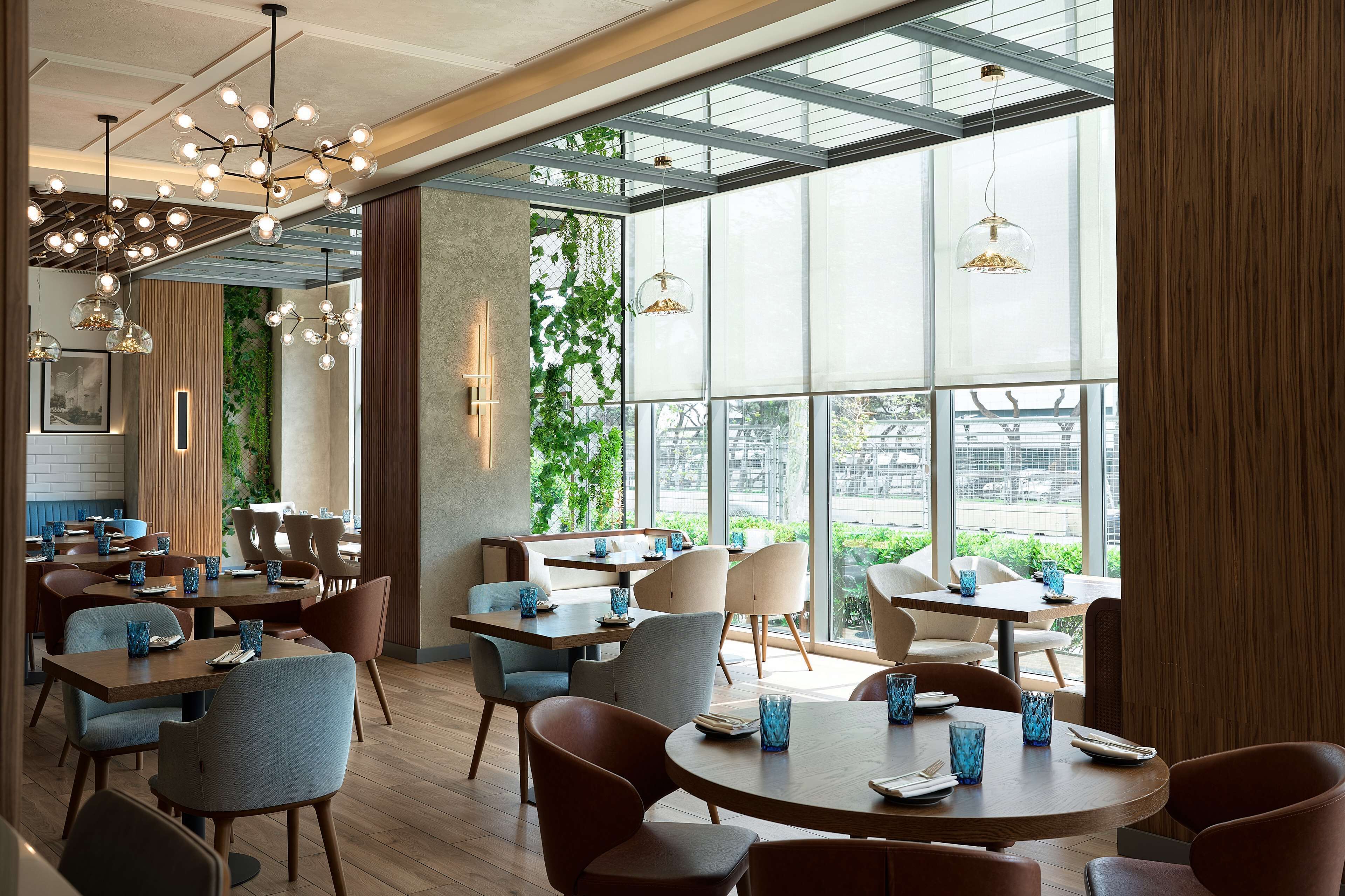 A modern restaurant interior with round tables, chairs, and hanging pendant lights.