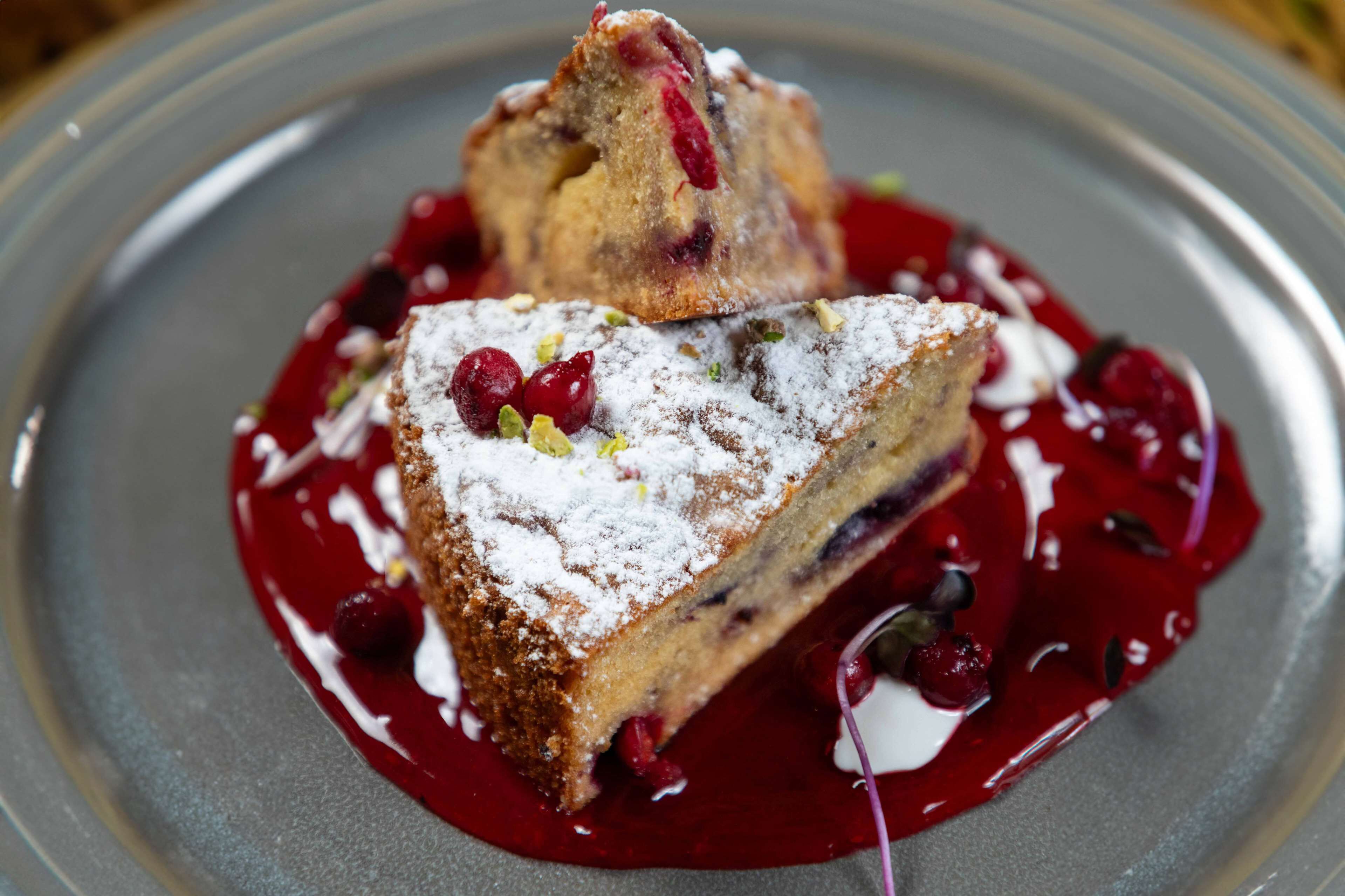 A dessert with a slice of cake topped with powdered sugar and berries, served on a plate with a red sauce.