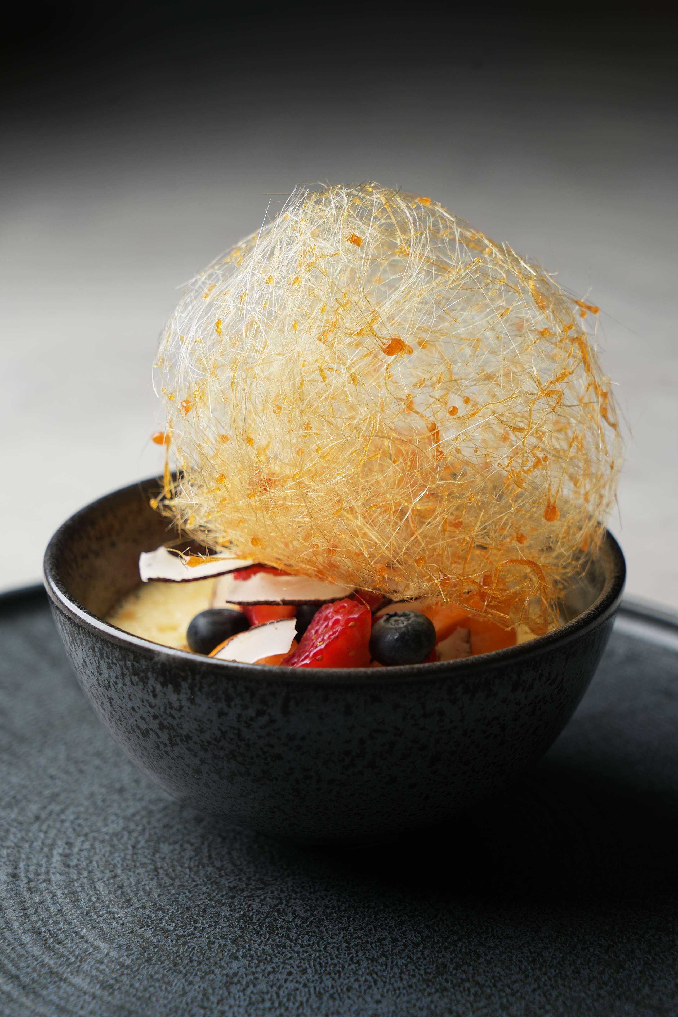 A bowl with a translucent, spherical object on top, containing various fruits and a white substance.