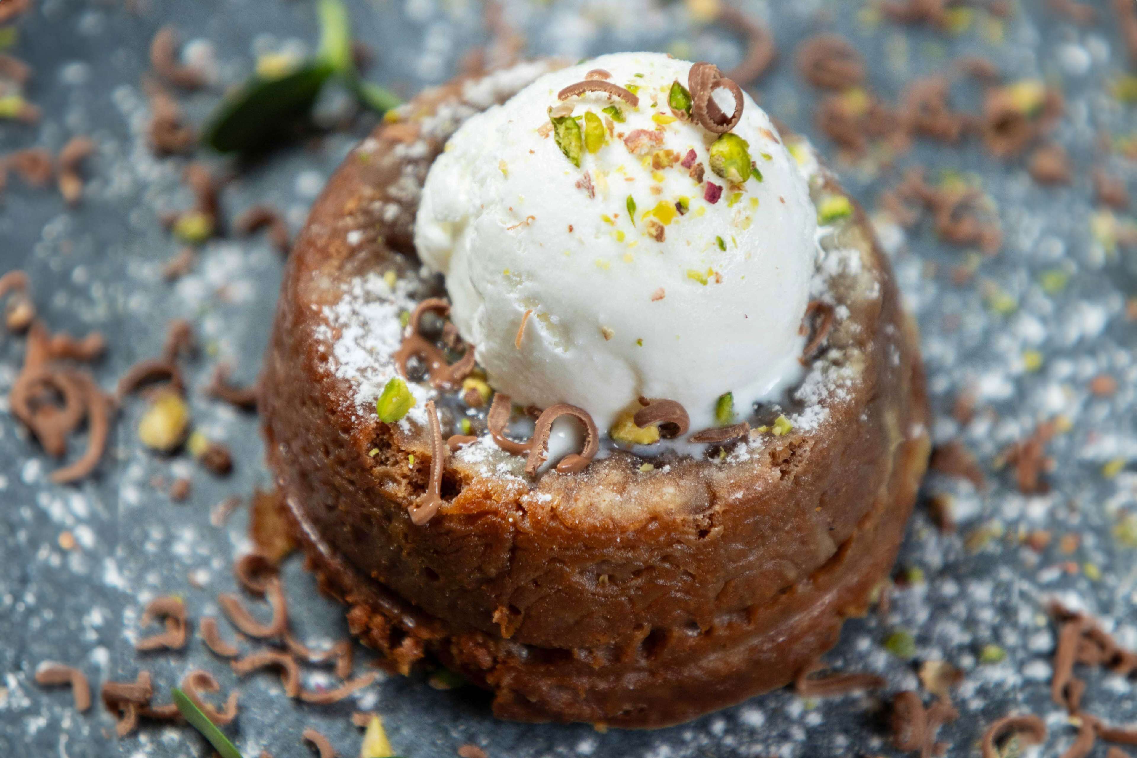 A dessert with a scoop of ice cream on top, garnished with nuts and sprinkled with powdered sugar.