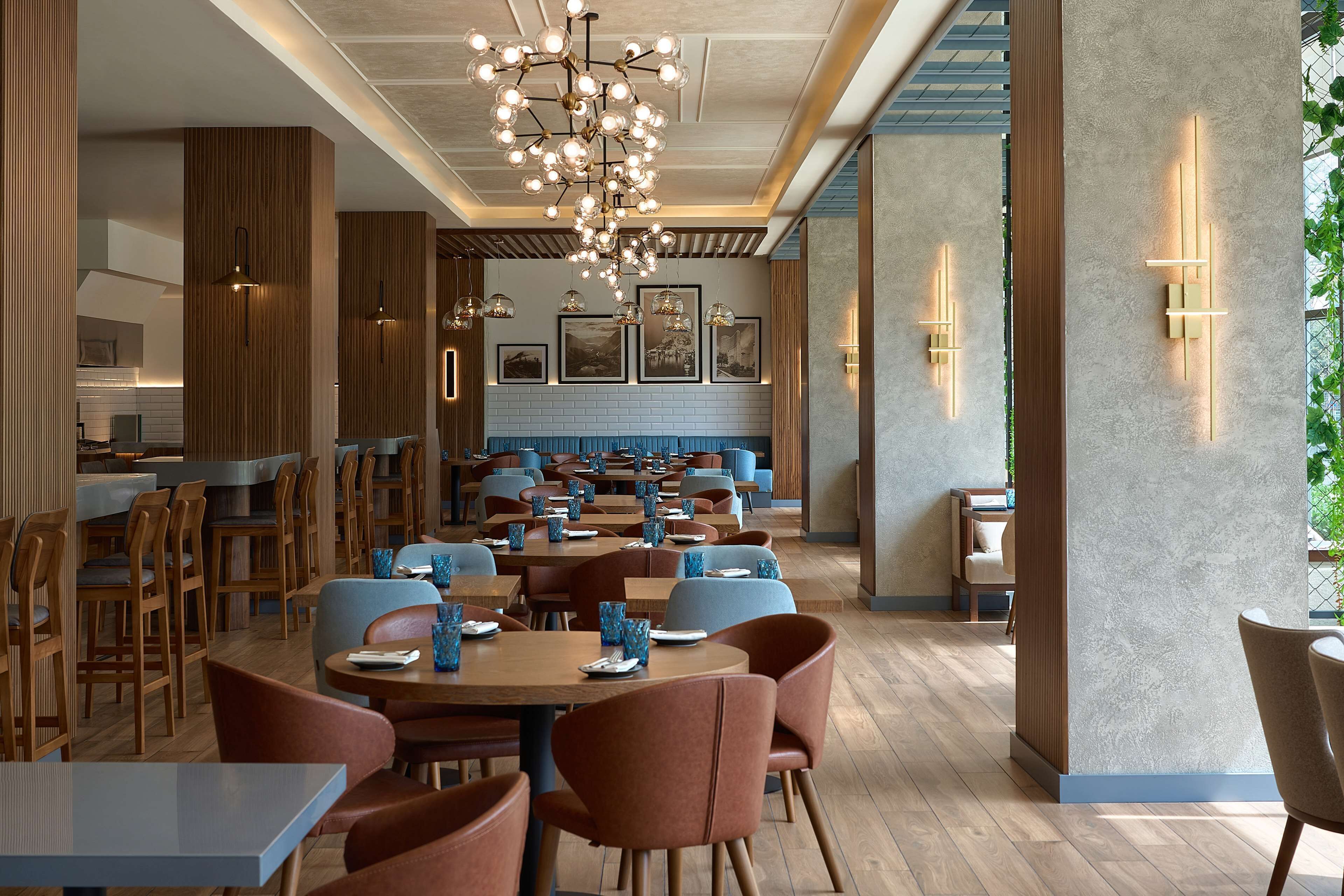 Un restaurant moderne avec des boiseries, des chaises bleues et brunes, et un lustre central. Les tables sont dressées avec de la vaisselle et des verres bleus.