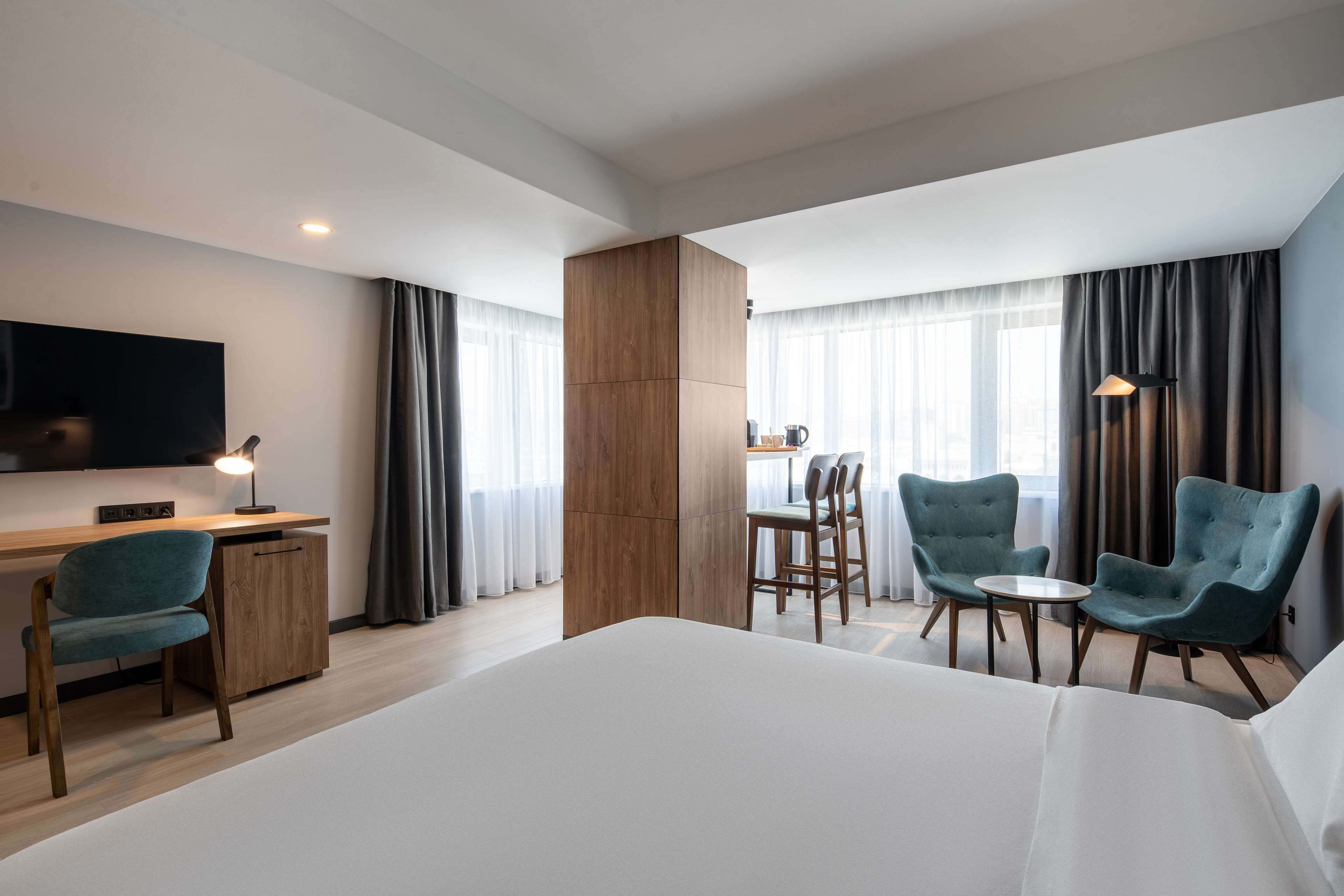 Camera d'albergo con un letto grande, una scrivania con una sedia, una televisione e due poltrone.