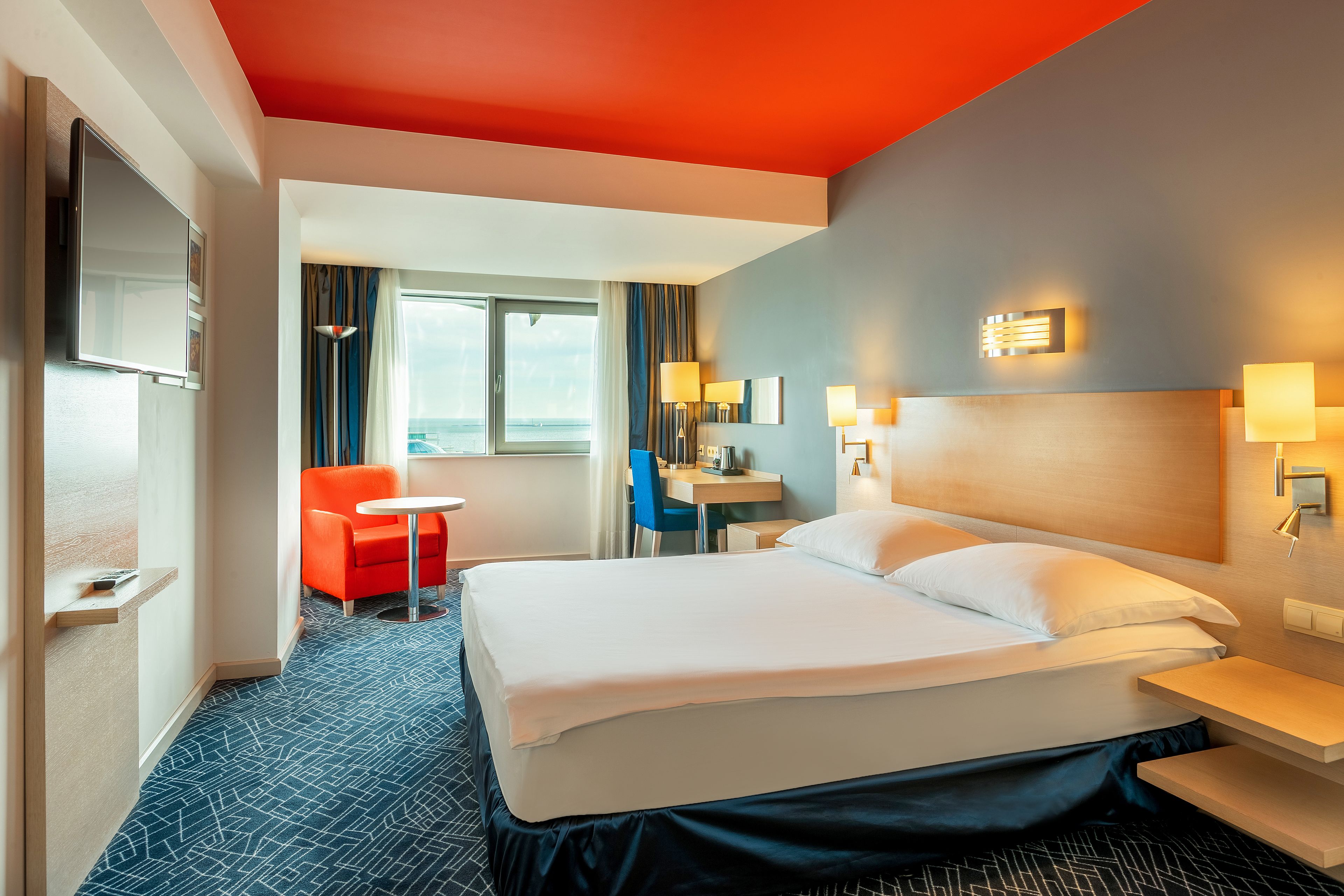 A hotel room with a large bed, a desk, a chair, and a TV.