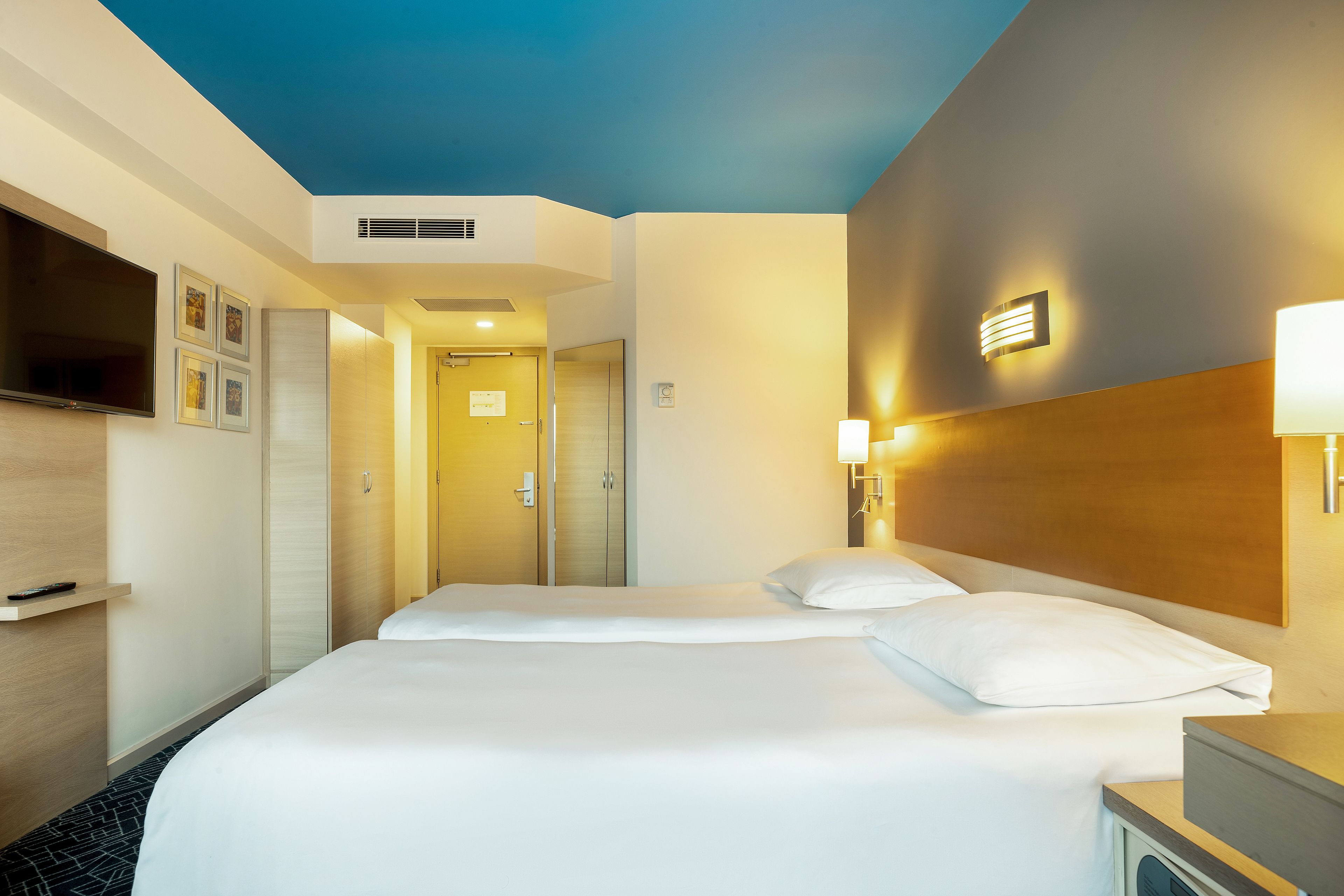 Une chambre d’hôtel avec deux lits, une télévision, un minibar et une porte de salle de bain.