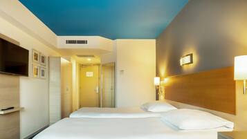 Une chambre d’hôtel avec deux lits, une télévision, un minibar et une porte de salle de bain.